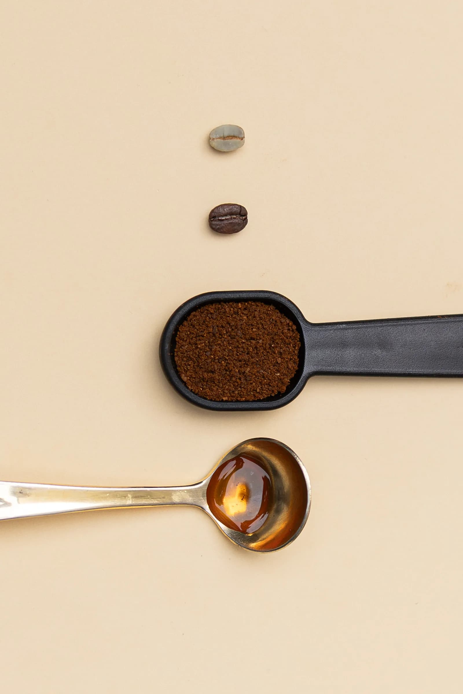 Colheres com café moído e grãos de café dispostas sobre fundo claro
